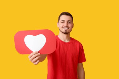 Sarı arkaplanda ikon gibi kalbi olan yakışıklı, mutlu genç bir adam.