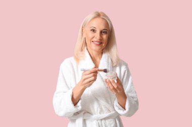 Bornozlu, makyajlı ve arka planda fırçası olan olgun bir kadın.