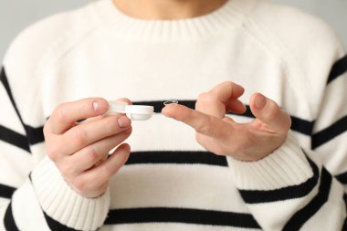 Kontak lensli olgun bir kadın ve gri arka planda bir çanta, yakın plan.