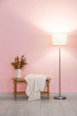 Modern parlayan lamba ve pembe duvarın yanındaki ahşap bank.