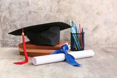 Harç tahtasıyla diploma, kitaplar ve gri arka planda farklı kırtasiye malzemeleri.