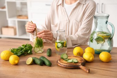 Genç kadın ve limonlu, salatalıklı ve naneli şişeler mutfaktaki masada.