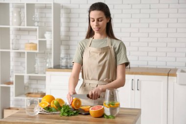 Mutfakta naneli su hazırlamak için turuncu kesen güzel genç bir kadın.
