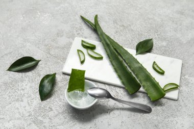 Bir kase aloe vera jeli ve gri arkaplanda yapraklar