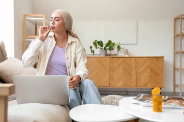 Kemoterapiden sonra dizüstü bilgisayarla kanepede ot içen genç bir kadın.