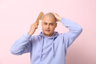 Pembe arka planda tarağı olan kel bir genç.