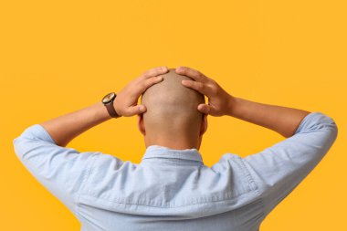 Gergin, kel, sarı arka planda genç bir adam.