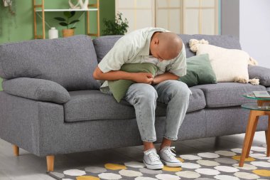 Apandisiti olan genç bir adam evdeki kanepede oturuyor.