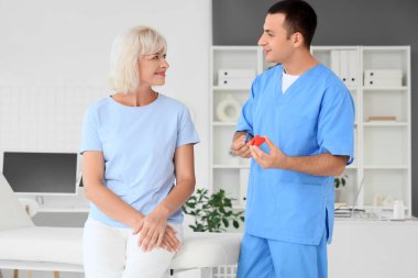 Erkek endokrinolog, klinikte olgun bir kadına tiroit bezi modeli gösteriyor.