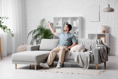 Yakışıklı delikanlı kanepede oturuyor ve oturma odasındaki klimayı açıyor.