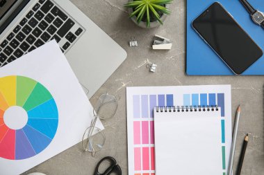 Gri grunge tablosunda dizüstü bilgisayarı, kalemleri ve renk çizelgeleri olan grafik tasarımcılarının çalışma yeri