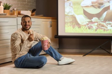 Patlamış mısırlı genç adam geceleri mutfakta projektör ekranında film izliyor.