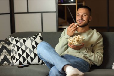 Patlamış mısırlı genç adam akşamları kanepede film izliyor.