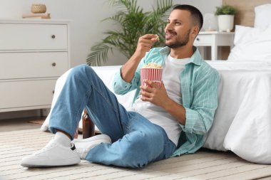Patlamış mısırlı genç adam yatak odasında film izliyor.