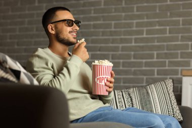 Üç boyutlu gözlüklü ve patlamış mısırlı genç adam akşamları evdeki kanepede film izliyor.