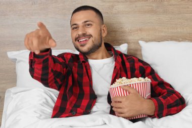 Patlamış mısırlı genç adam yatakta film izliyor.
