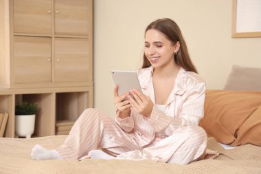 Evde pijamalı, tabletle sohbet eden genç ve güzel bir kadın.