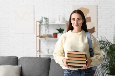 Güzel, mutlu, sırt çantası ve kitap yığınlarıyla dolu bir kız öğrenci.
