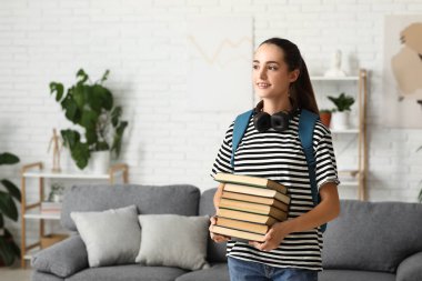 Evde kitap, çanta ve kulaklık yığını olan güzel, mutlu bir bayan öğrenci.