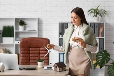 Ofiste kumbarası ve rüzgar türbini modeli olan kadın mühendis.