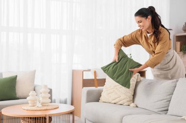Evdeki kanepede yastık ayarlayan genç bir kadın.