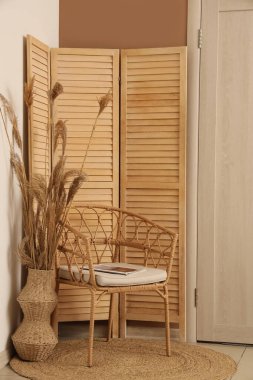 Modern koridorun içinde katlanan ekran, koltuk ve bej duvarın yanında kuru kamış vazosu var.