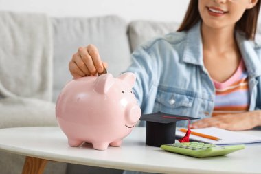 Bayan öğrenci masadaki kumbaraya para koyuyor, yakın plan. Eğitim tasarruf kavramı