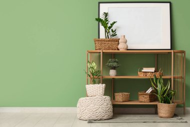 Raflar, ev bitkileri, pouf ve çerçeve yeşil duvarın yanında.