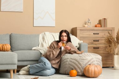 Sonbahar günü evde yeşil çay içen ve puf üzerine yaslanan genç bir kadın.