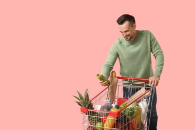 Pembe arka planda alışveriş arabası olan mutlu genç bir adam.