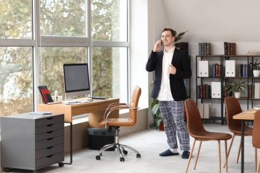 Ofiste cep telefonuyla konuşan genç bir işadamı. Ulusal İş Günü Pijamalarınızı Giyin