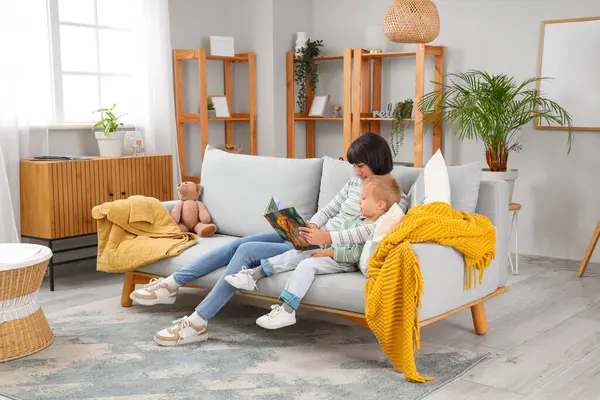 Genç anne ve küçük oğlu evdeki kanepede masal okuyorlar.