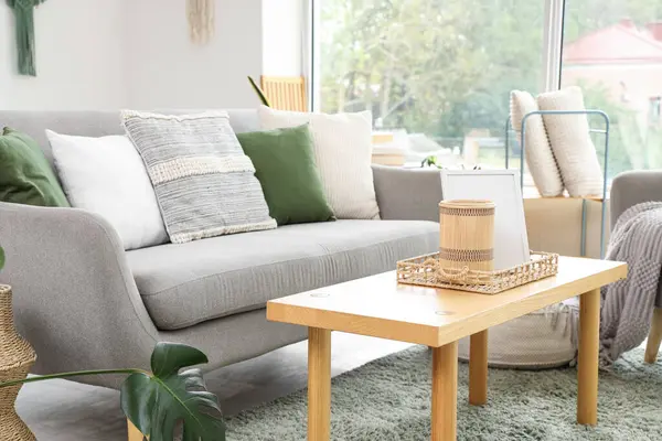 Gri kanepeli, kahve masalı, koltuklu ve pencereli aydınlık oturma odasının içi.