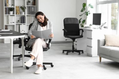 Ofiste cep telefonuyla konuşan dosyasıyla genç bir iş kadını. Ulusal İş Günü Pijamalarınızı Giyin