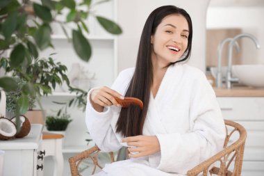 Kozmetik ürünleri ve Hindistan ceviziyle güzel, genç bir kadın banyoda saçını tarıyor.