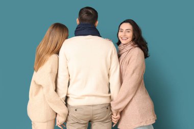 Sonbahar elbiseli iki erkek ve iki güzel kadın mavi arka planda el ele tutuşuyorlar. Poliyamory konsepti