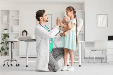 Erkek çocuk doktoru, klinikte oyuncak ayılı güzel bir kıza beşlik çakıyor.
