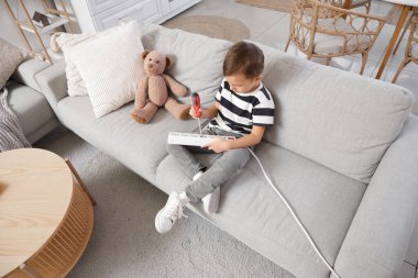 Evdeki kanepede tornavida ve uzatma kablosuyla oynayan sevimli küçük çocuk. Çocuk tehlikede.