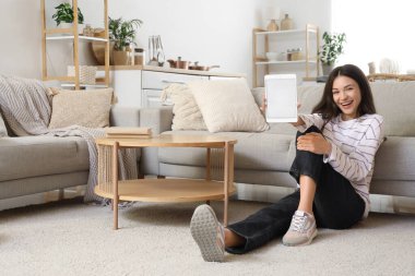 Evdeki halıda boş tabletli güzel bir kadın oturuyor.