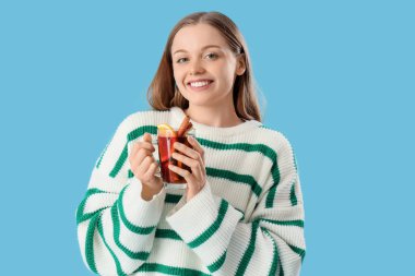 Mavi arka planda cam bardak sıcak şarap ile güzel genç bir kadın.