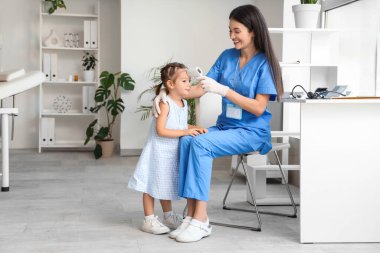 Kızılötesi termometresi olan kadın bir çocuk doktoru klinikte küçük bir kızın ateşini ölçüyor.