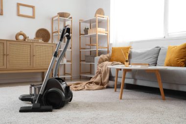 Elektrikli süpürge, kanepe ve klozetle aydınlık oturma odasının içinde.