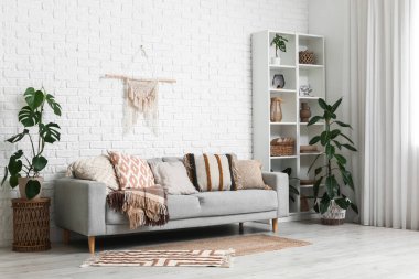 Oturma odasının içinde rahat bir kanepe, raf ünitesi ve çiçekleri var.