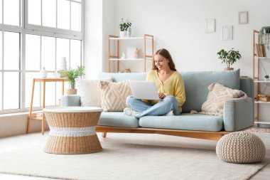 oturma odasında kanepede otururken dizüstü kullanarak güzel bir genç kadın