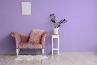 Mor duvarın yanındaki taburede şık bir kanepe ve çiçek var.