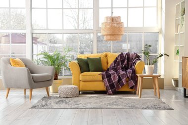 Modern oturma odasının içinde, koltuğu, çiçekleri ve pencerenin yanındaki sarı kanepede mor ekoseli.