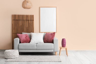 Modern oturma odasının içi. Gri kanepenin üzerinde katlanan ekran, boya ve mor yastıklar var.