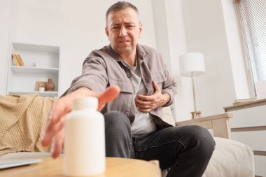 Göğüs ağrısı çeken olgun bir adam. Evdeki masadan ilaç alıyor.