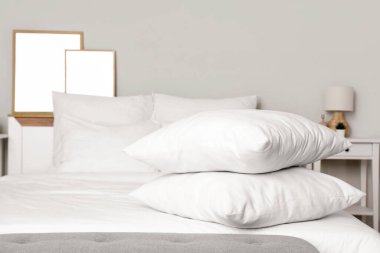 Beyaz battaniyeli rahat yatak ve şık yatak odasında yumuşak yastıklar, yakın çekim.