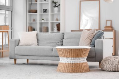 Aydınlık oturma odasının içinde gri kanepe, rattan masa ve raf ünitesi var.